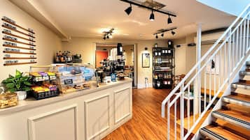 A café with a counter displaying various coffee options and pastries, a staircase, and a shelving unit with beverages.