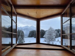 Ein Zimmer mit großen Fenstern und Blick auf verschneite Berge und Bäume.