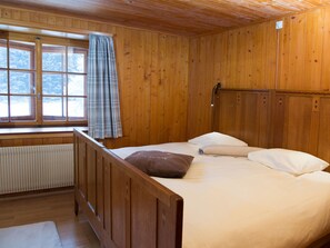 Ein Zimmer in einer Holzhütte mit einem Bett, einem Fenster mit Vorhängen und einer Heizung.