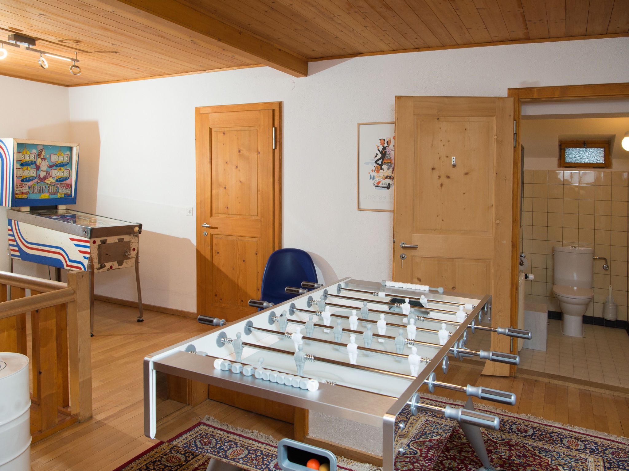 Une pièce avec une table de baby-foot, une chaise bleue, des portes en bois et une petite fenêtre.