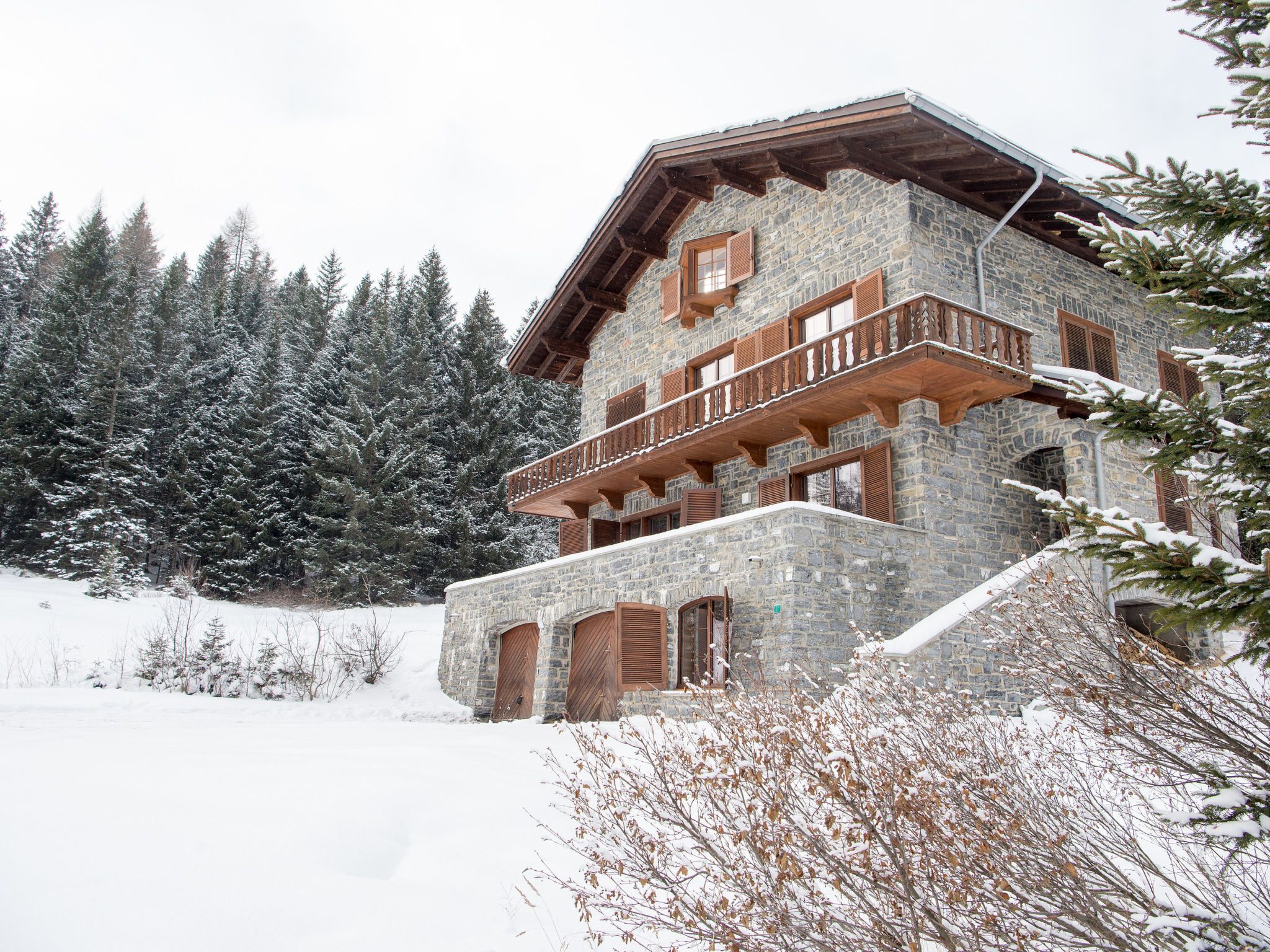 A stone building with a wooden balcony, surrounded by snow-covered trees.