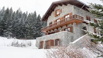 A stone building with a wooden balcony, surrounded by snow-covered trees.
