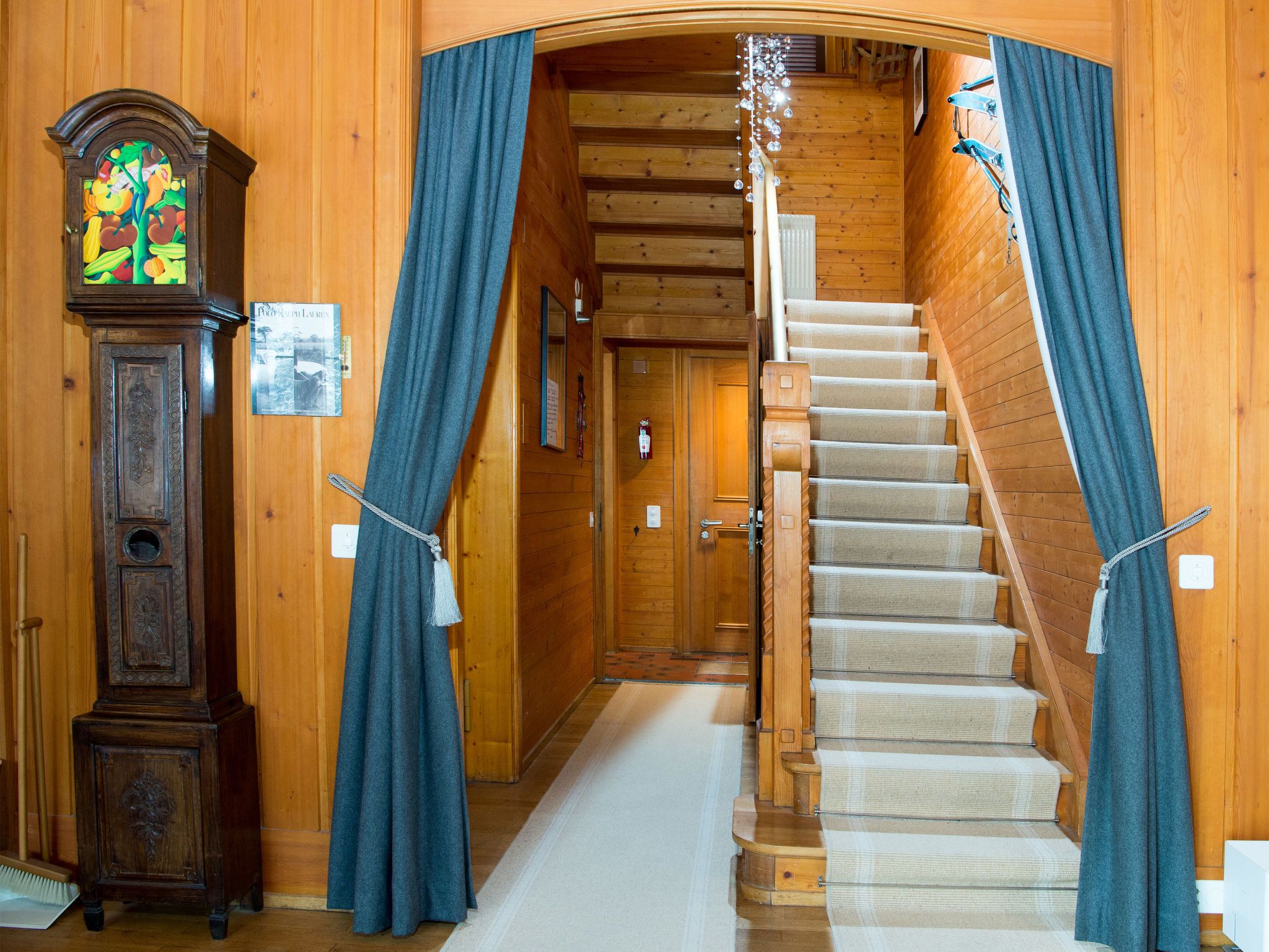 Un intérieur en bois avec un escalier, une horloge murale et des rideaux.
