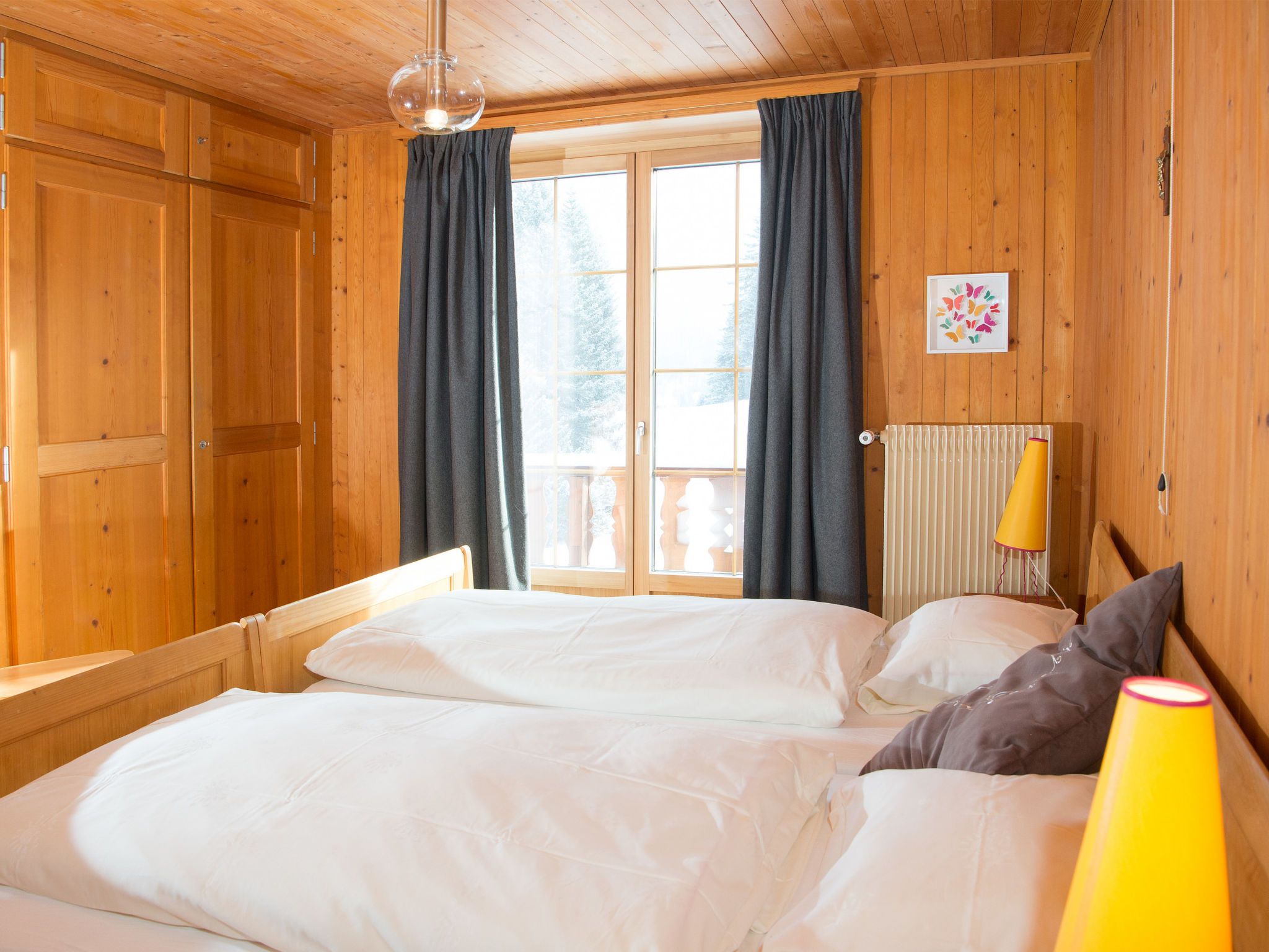 A wooden cabin room with a bed, curtains, a window, and a radiator.