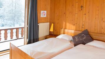 Habitación de cabaña de madera con una cama, una ventana con cortinas, un radiador y una lámpara fijada a la pared.