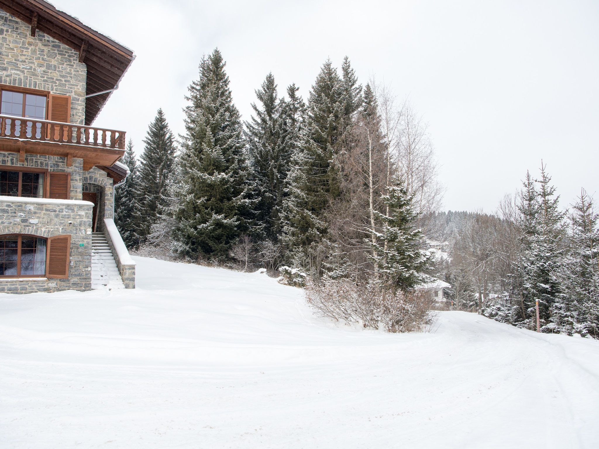 A stone building with a wooden balcony, surrounded by snow-covered trees.