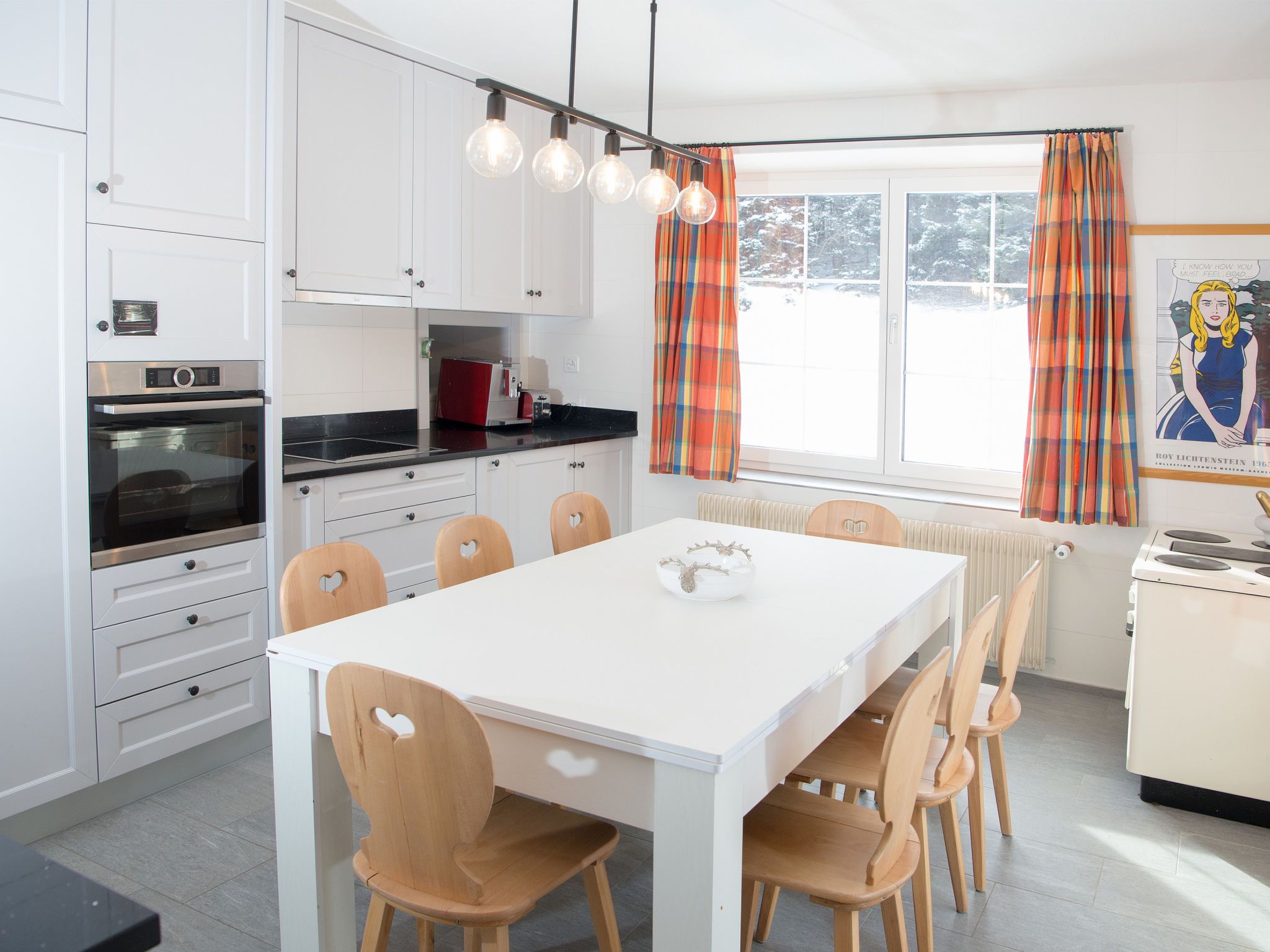 Une cuisine moderne avec des meubles blancs, un plan de travail noir et une table à manger blanche, assortie de chaises en bois.