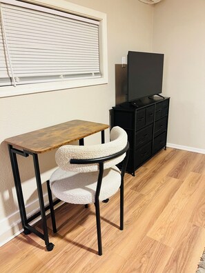 Quarto com escrivaninha de madeira, uma cadeira, cômoda preta e televisão por cima.