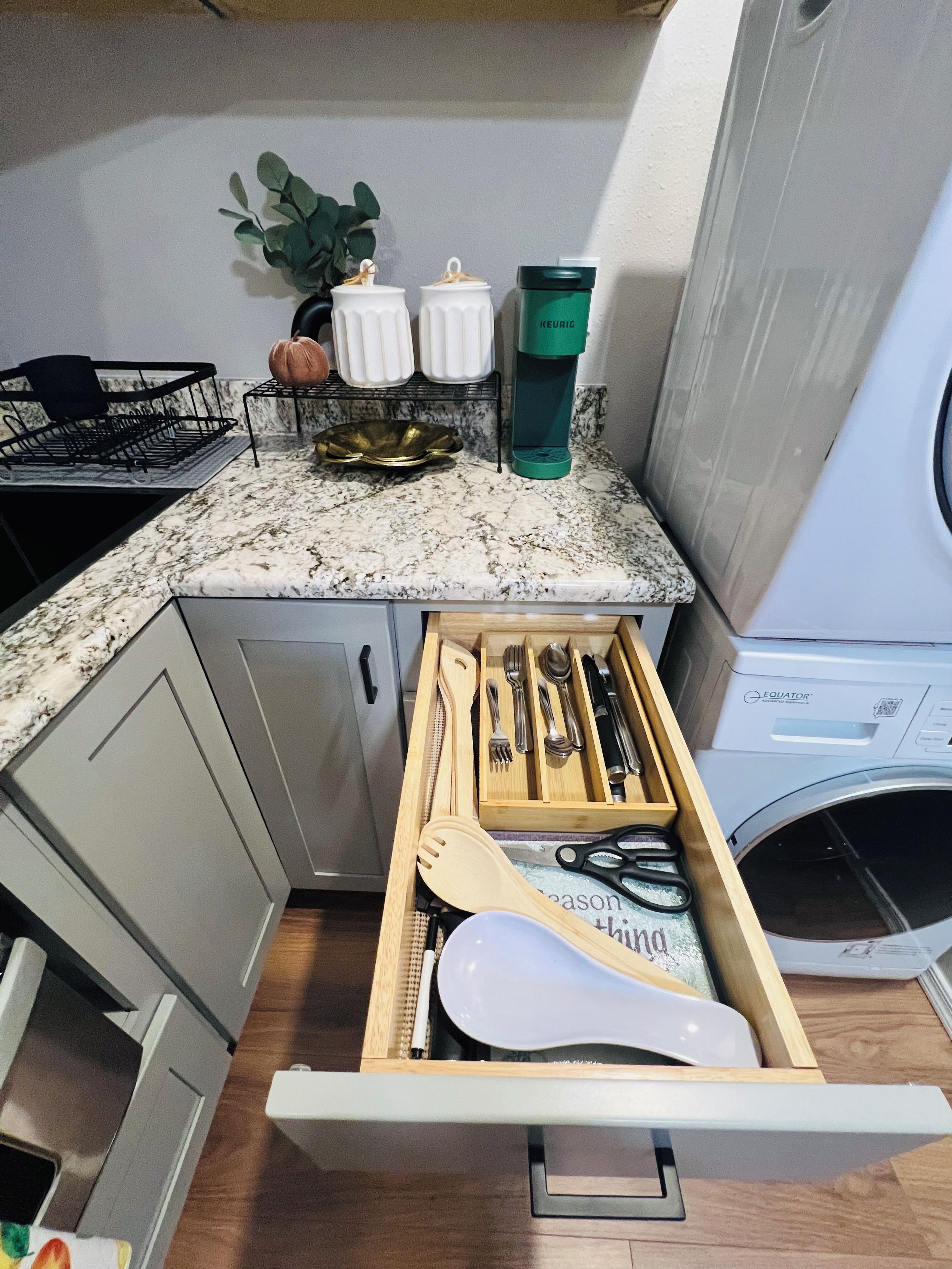 A kitchen with a drawer organizer containing utensils, a coffee maker, and a dish rack.