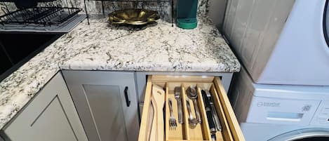 Una cocina con un organizador de cajones que contiene utensilios, una cafetera y un escurreplatos.