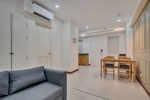 Un soggiorno moderno con un divano grigio, un'area pranzo con sedie di legno e un tavolo, e una cucina sullo sfondo.