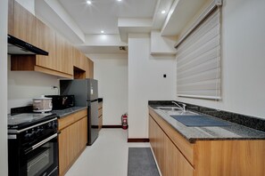 A modern kitchen with wooden cabinets, a stainless steel refrigerator, a stove, and a granite countertop. - Luxury 2BR Condo in Taguig | Free Parking & Balcony (Taguig)