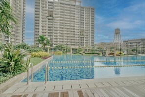 A swimming pool with clear blue water, surrounded by greenery and modern buildings. - Luxury 2BR Condo in Taguig | Free Parking & Balcony (Taguig)