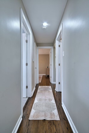 A hallway with white walls, wooden flooring, and a patterned rug. - Your Chicago Home Between Homes - 4BR Furnished Home (Chicago)