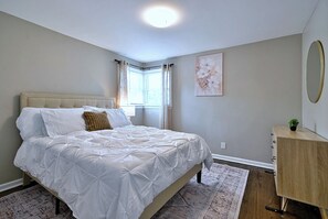 A bedroom with a bed, a window with curtains, a painting on the wall, and a dresser. - Your Chicago Home Between Homes - 4BR Furnished Home (Chicago)