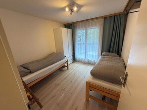 A small room with two beds, a wardrobe, and a window with curtains. - Am Bächli Appartement/Fewo 4-Bettwohnung by Interhome (Engelberg)