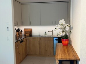 Eine moderne Küche mit Holzschränken, einer schwarzen Arbeitsplatte und einem Holztisch mit Orchidee im Topf.