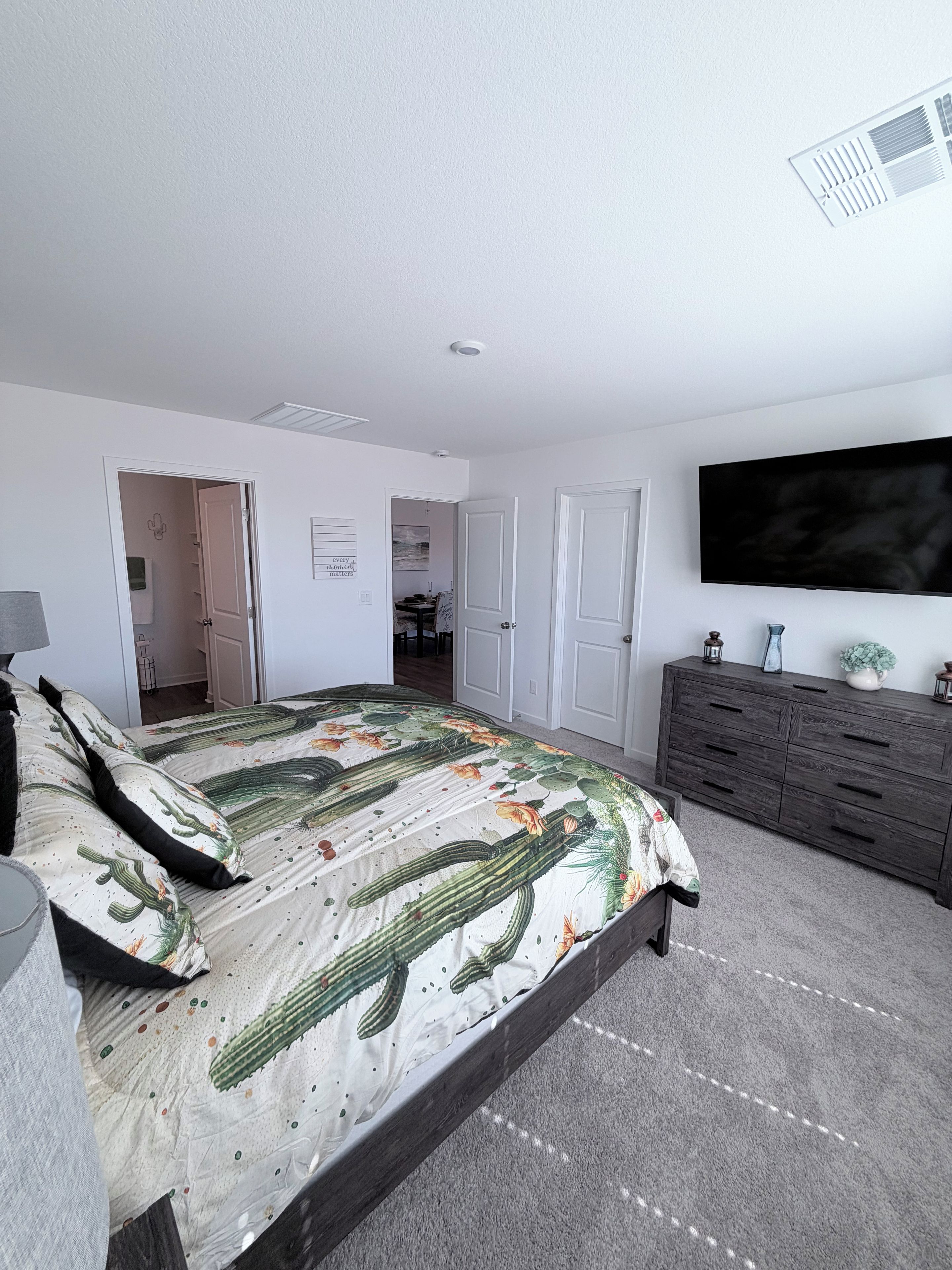 A bedroom with a bed, a dresser, a television, and a door leading to another room.