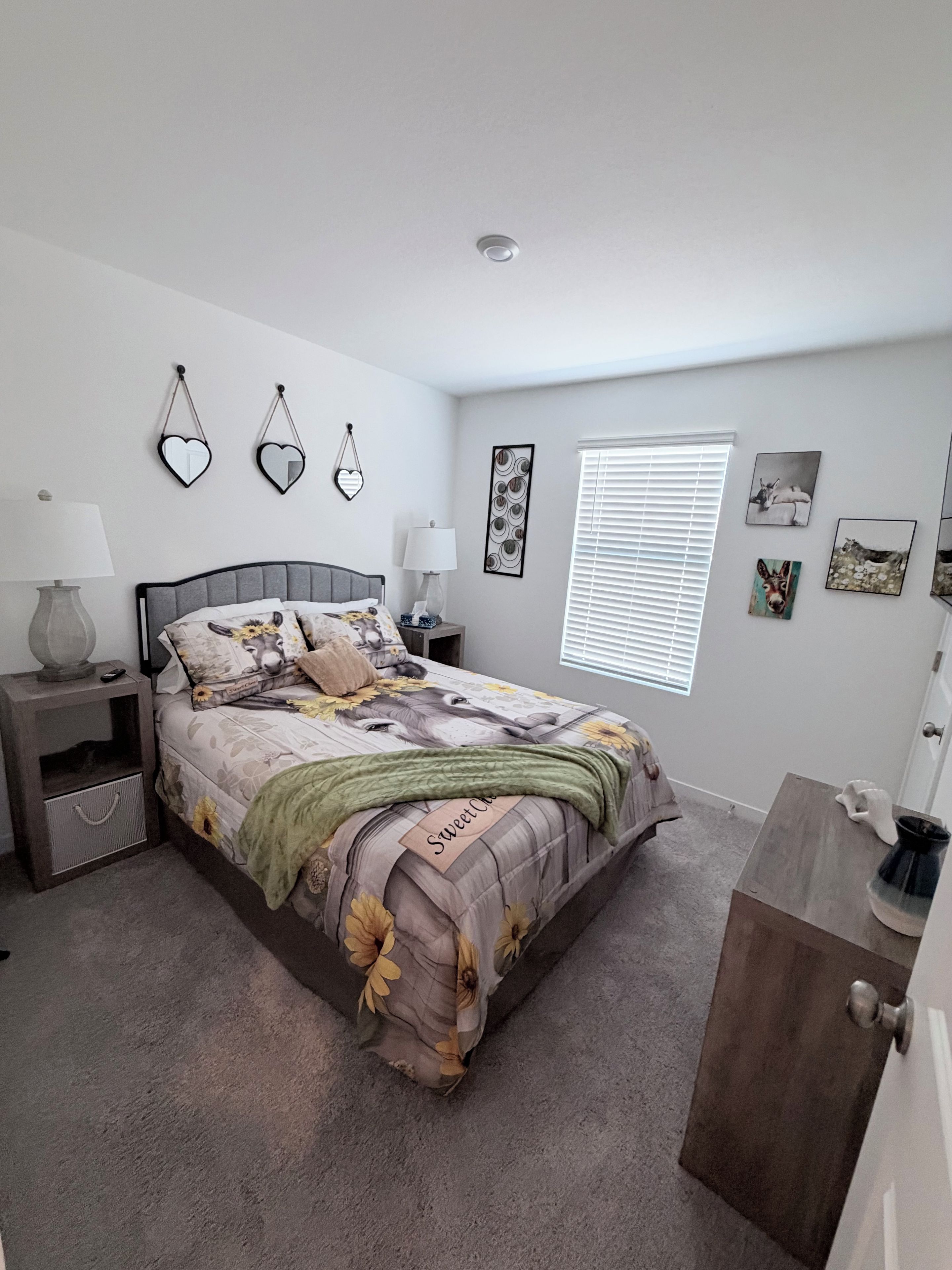 A bedroom with a bed, nightstands, a dresser, a window with blinds, and wall art.