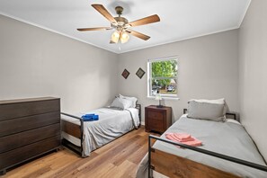 Un dormitorio con dos camas individuales, un aparador de madera, un ventilador de techo y una ventana con vista al exterior.