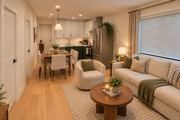 Ein modernes Wohnzimmer mit einer Couch, Sesseln, einem Couchtisch und einem Essbereich mit Tisch und Stühlen.