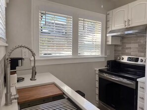 Eine Küche mit Backofen, einer Kaffeemaschine und einem Fenster mit Jalousien.