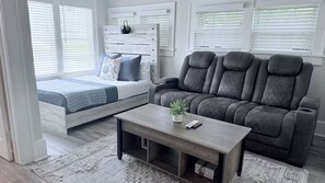 A bedroom with a bed, a gray sofa, a wooden coffee table, and a window with blinds. - Cozy Nook in Saint Petersburg (St. Petersburg)