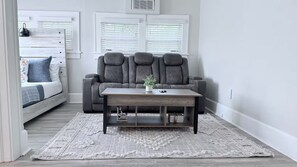 Uma sala de estar moderna com um sofá cinzento, uma mesa de centro de madeira e um tapete estampado.