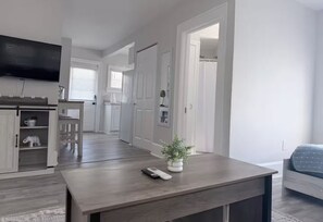 Eine moderne Küche mit weißen Schränken, ein Essbereich mit Tisch und Stühlen sowie ein Wohnzimmer mit einer Couch.