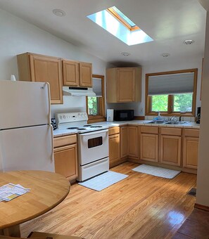 A kitchen with wooden cabinets, a white refrigerator, a stove, and a skylight. - Cozy 2-bedroom house in a woodsy setting, near restaurants, shops, and more. (Pontiac)