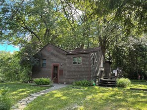 Ein rustikales Holzhaus mit einer Veranda, umgeben von üppigem Grün und Bäumen.