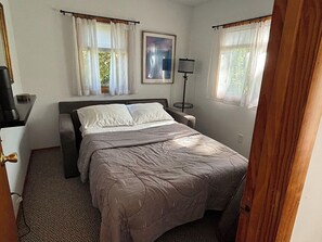 Ein Schlafzimmer mit einem Bett, einem Nachttisch, einer Lampe und einem gerahmten Bild an der Wand.