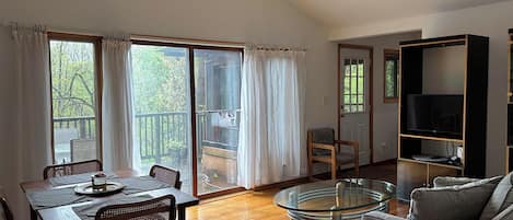 A spacious living area with a dining table, chairs, a glass coffee table, a sofa, and a television.