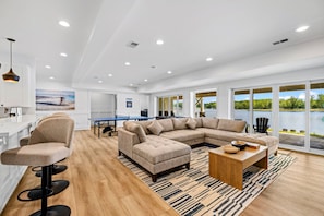 A spacious living area with a large sectional sofa, a ping pong table, and a view of a lake through large windows. - Lakefront Lake Anna | Theater, Hot Tub, Beach (Mineral)