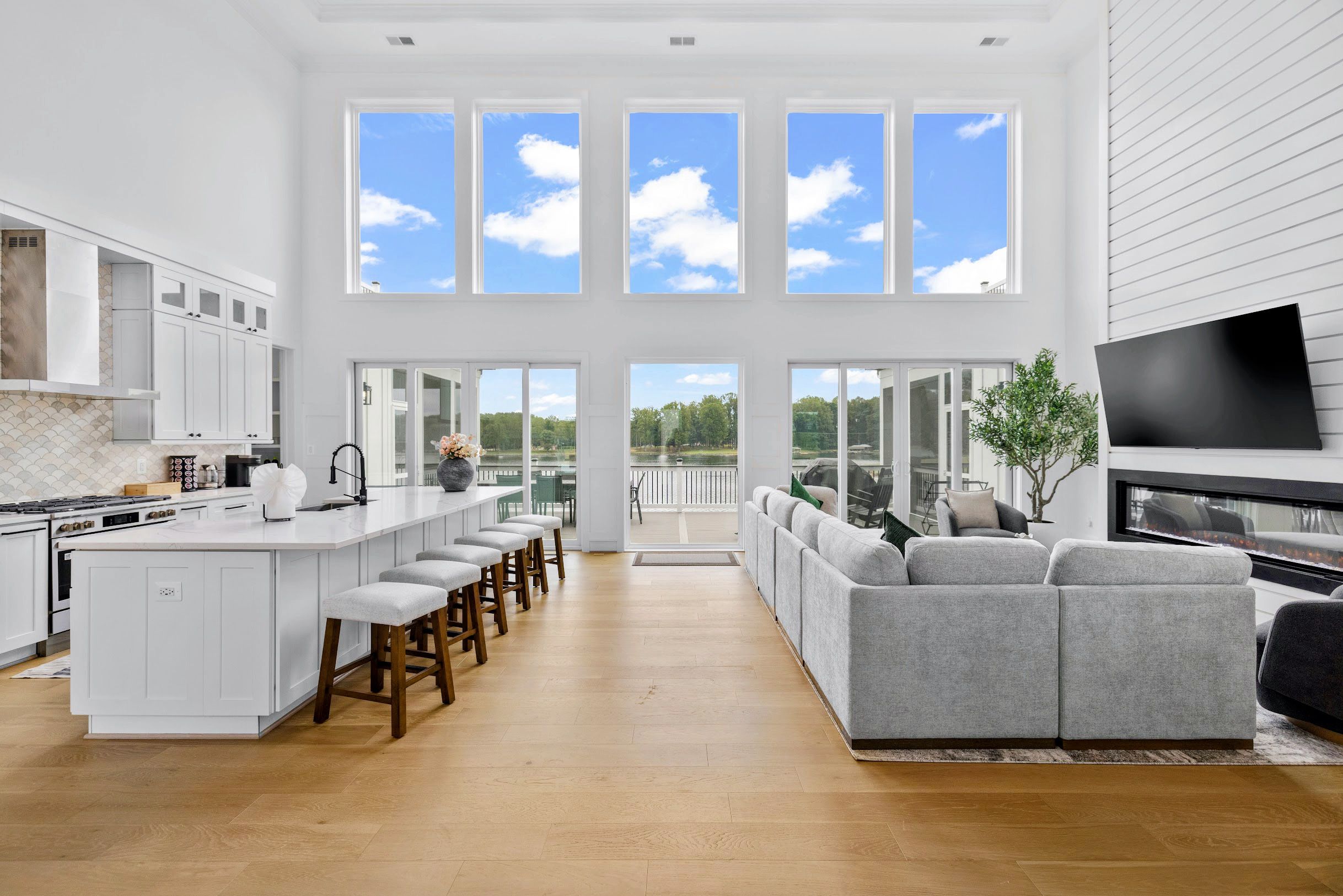 A spacious kitchen with a central island, a dining area with a grey sofa, and a large TV.