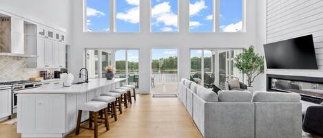 A spacious kitchen with a central island, a dining area with a grey sofa, and a large TV.