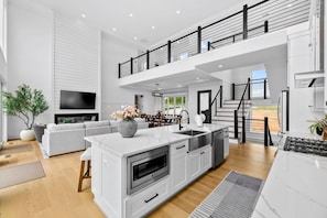 A modern kitchen with a central island, a dining area with a sofa, and a staircase leading to an upper level. - Lakefront Lake Anna | Theater, Hot Tub, Beach (Mineral)