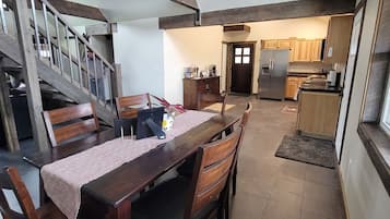 A dining area with a wooden table and chairs, a staircase, and a kitchen in the background.
