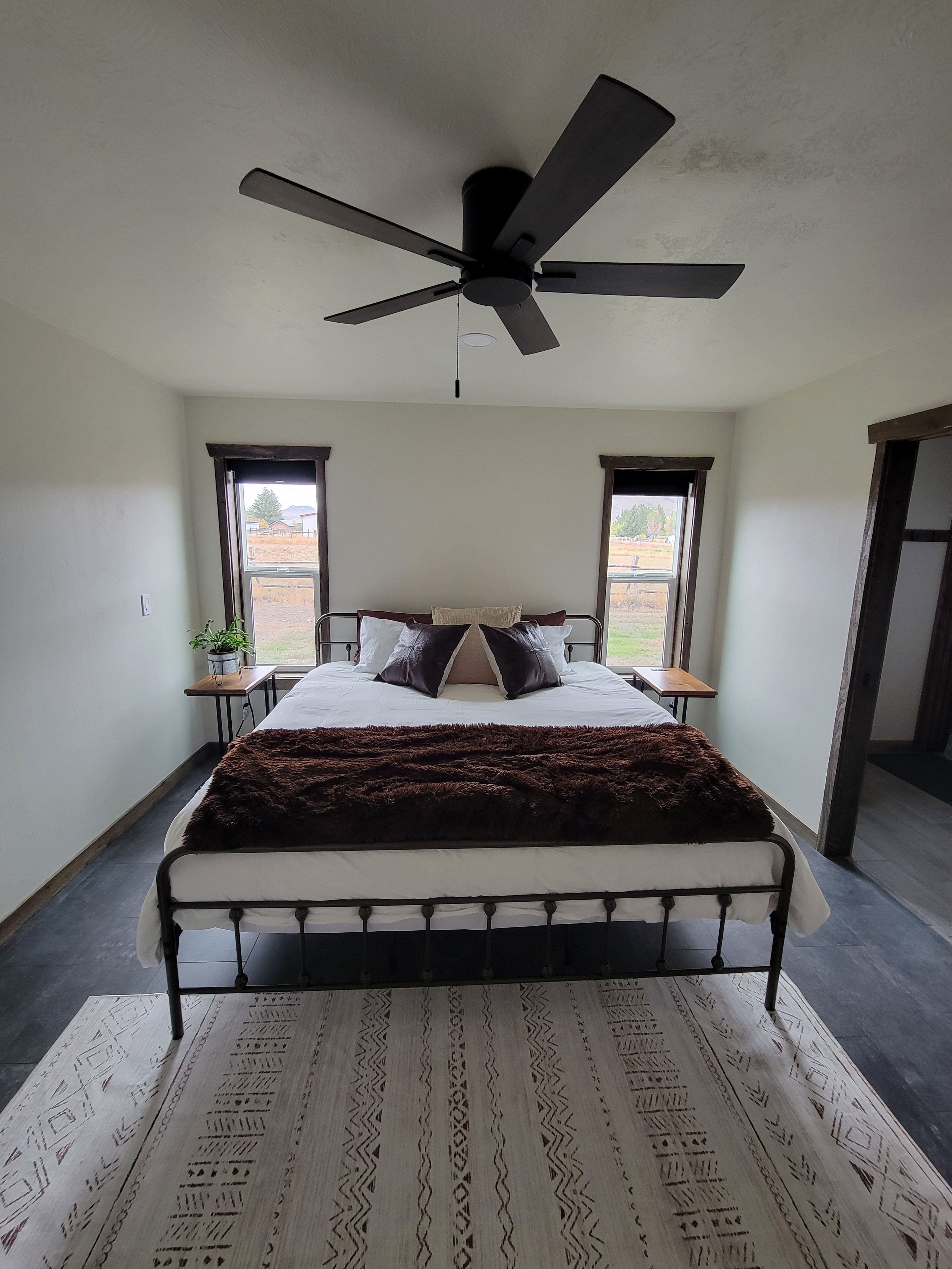 A bedroom with a bed, a ceiling fan, a window, and a door.