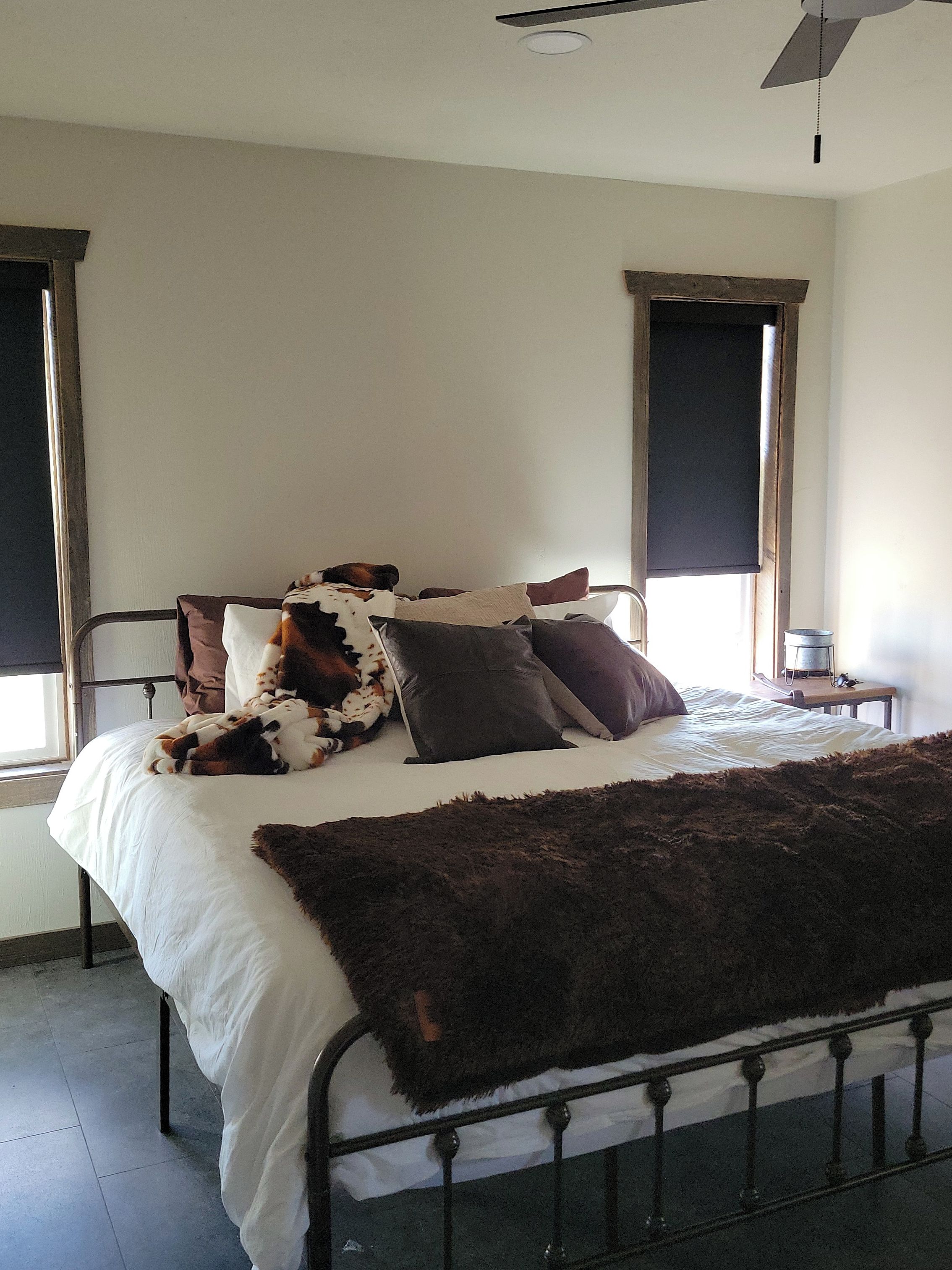Un lit avec un matelas blanc, une couverture en fausse fourrure marron et plusieurs oreillers, dont un à motifs de vaches.