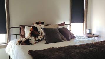 Un lit avec un matelas blanc, une couverture en fausse fourrure marron et plusieurs oreillers, dont un à motifs de vaches.