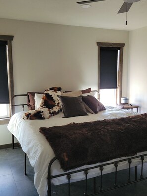 A bed with a white mattress, a brown furry throw blanket, and several pillows, including a cow-patterned one.