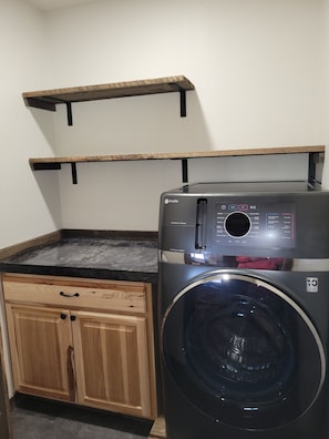 A compact laundry area with a front-loading washer and dryer, wooden cabinets, and a small shelf above the washer.