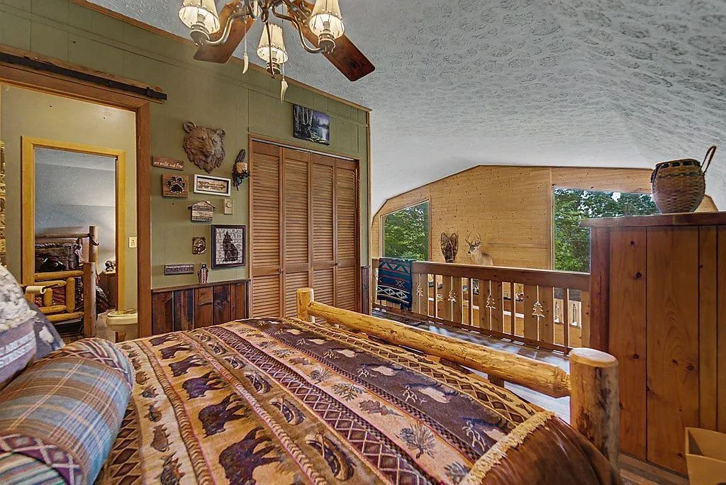 A bedroom with a large bed, wooden headboard, a balcony with a view, and a ceiling fan.