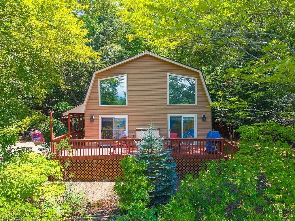 A two-story house with a deck, surrounded by dense greenery.