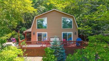 A two-story house with a deck, surrounded by dense greenery.