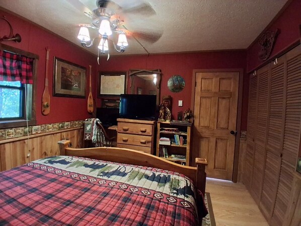 A bedroom with a bed, wooden dresser, and a television.