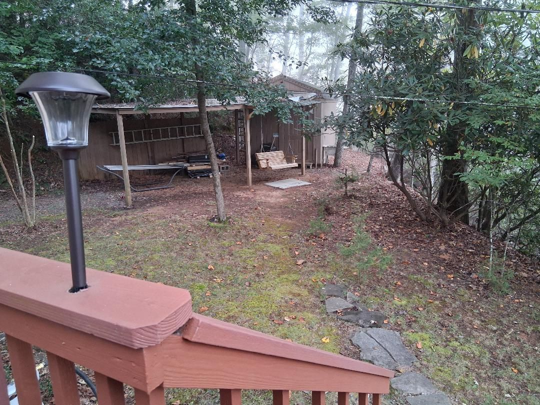 A wooden deck with a metal lamp post, a wooden swing set, and a small shed in a wooded area.