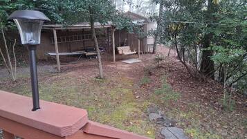 A wooden deck with a metal lamp post, a wooden swing set, and a small shed in a wooded area.