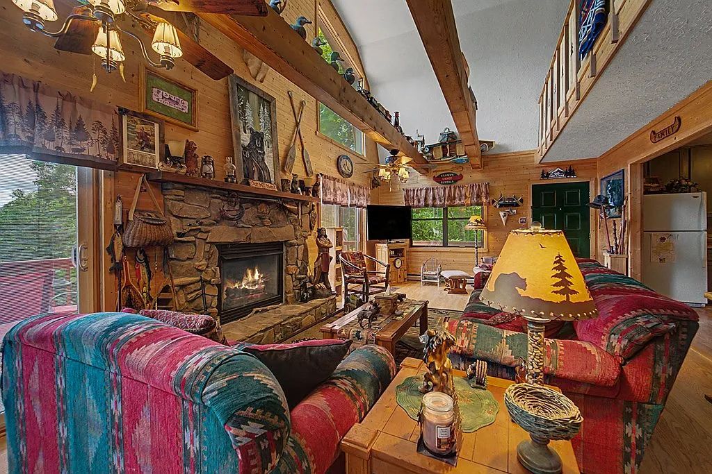 A cozy cabin interior with a stone fireplace, wooden beams, and colorful furnishings.